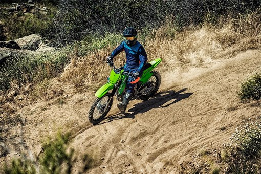Front three-quarter right view of a person riding a green dirt bike off-road. opens in a new window