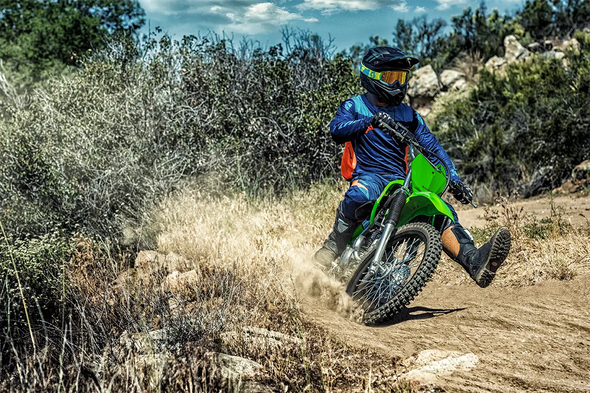 Oncoming image of a person riding a dirt bike with one foot out.