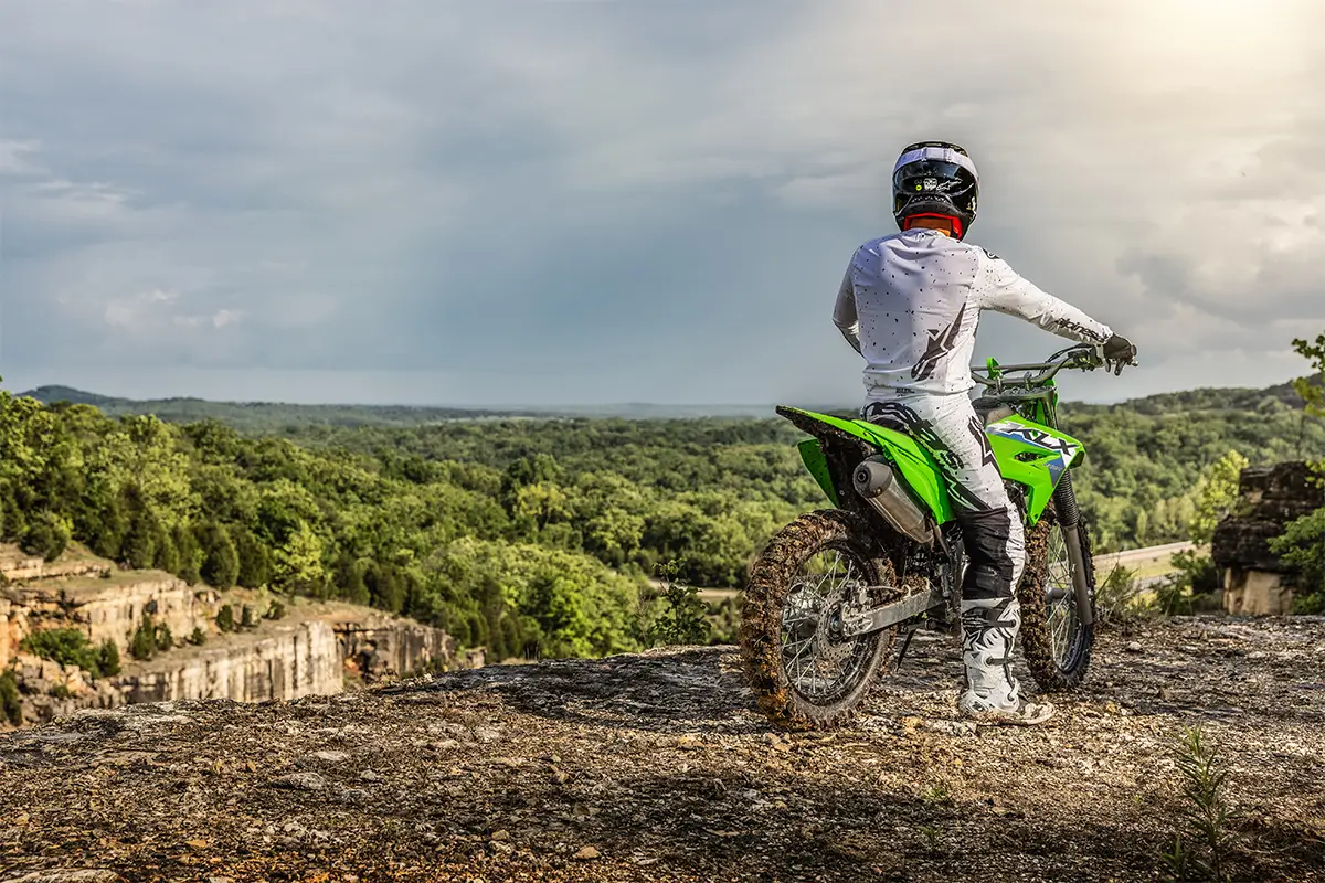 Three-quarter rear angle of a person seated on a motorcycle off-road.