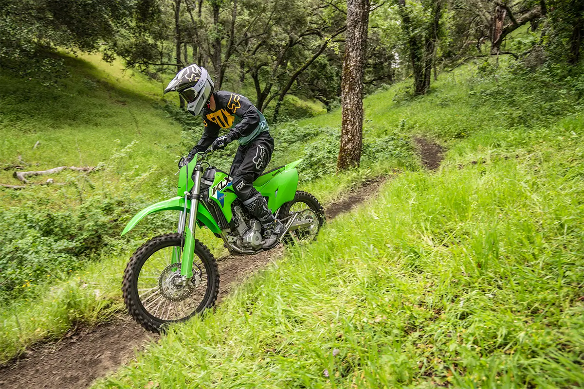 A person riding a green off-road dirt bike down a trail in a green forest.