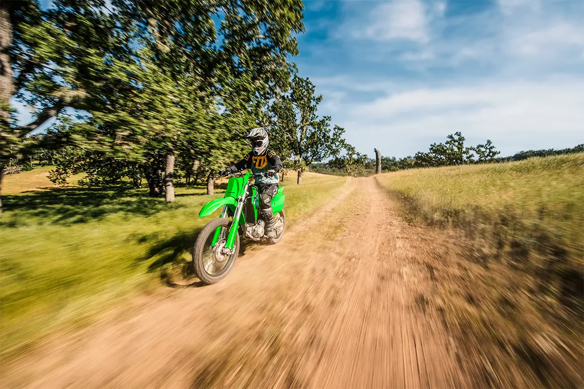 Oncoming view of a person riding a green off-road dirt bike down a dirt road.