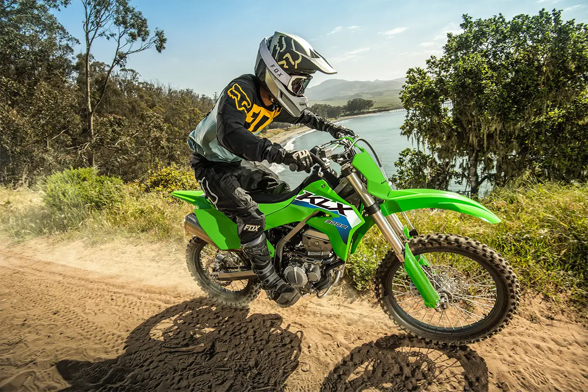 Right side view of a person riding a green dirt bike down a scenic trail overlooking the ocean.