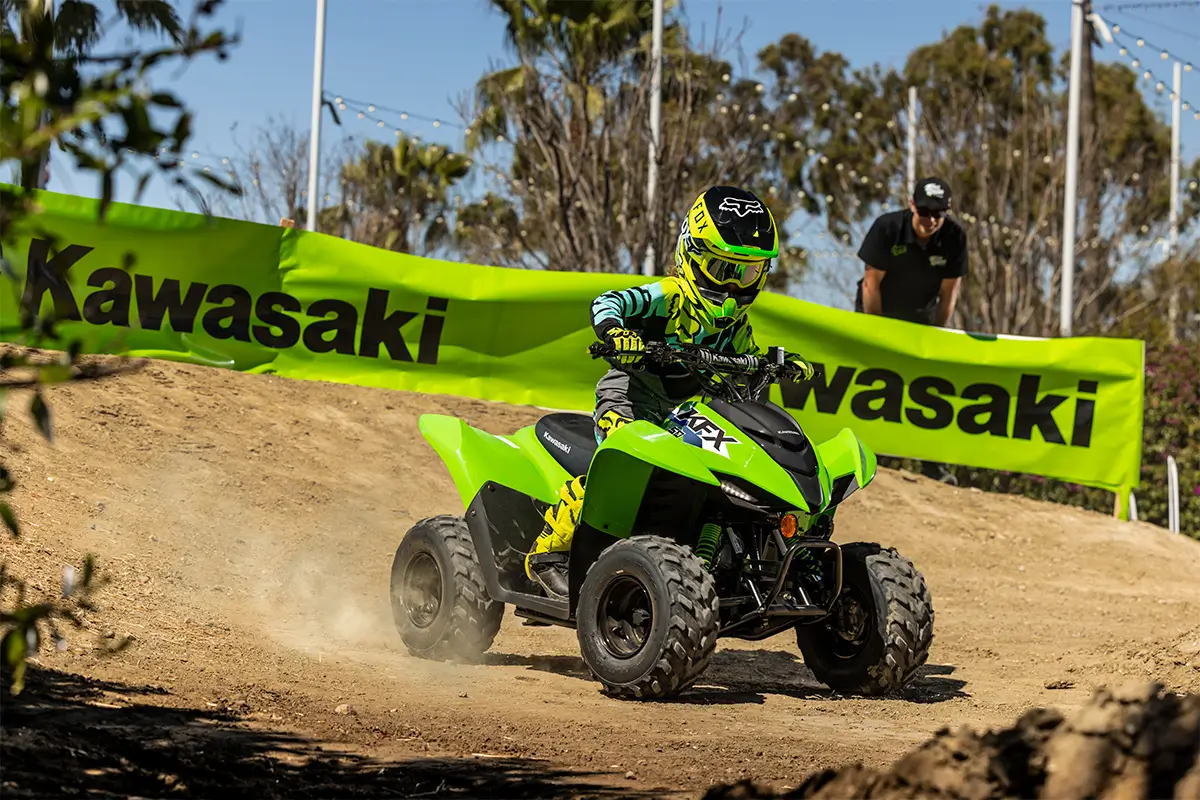 A kid riding a green youth ATV on a motocross track.