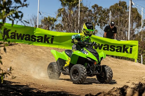A kid riding a green youth ATV on a motocross track. opens in a new window