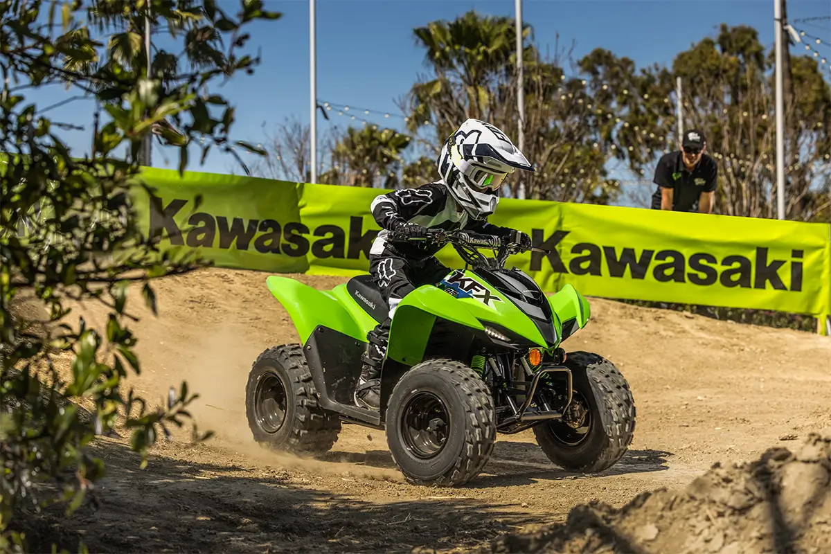 A kid riding a green youth ATV on a motocross track.