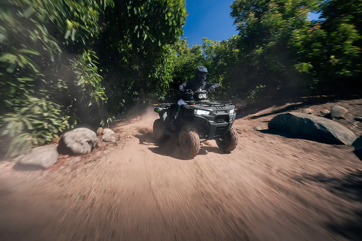 A person riding fast on a utility ATV on a road through an orchard.