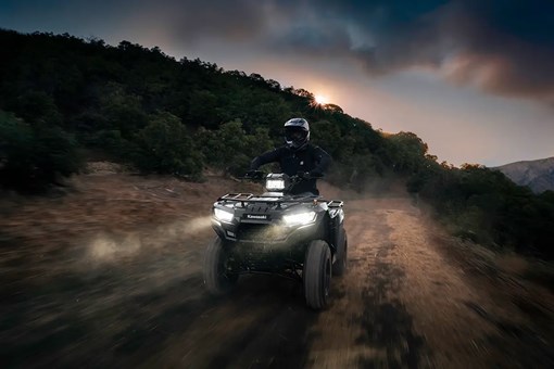A person riding a utility ATV on a dusty road at night with headlights on. opens in a new window
