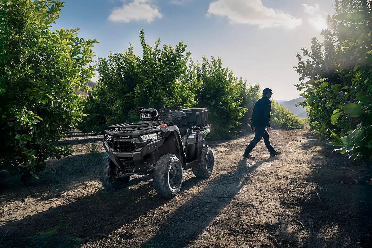 A utility ATV parked in an orchard with a person in the background walking away.