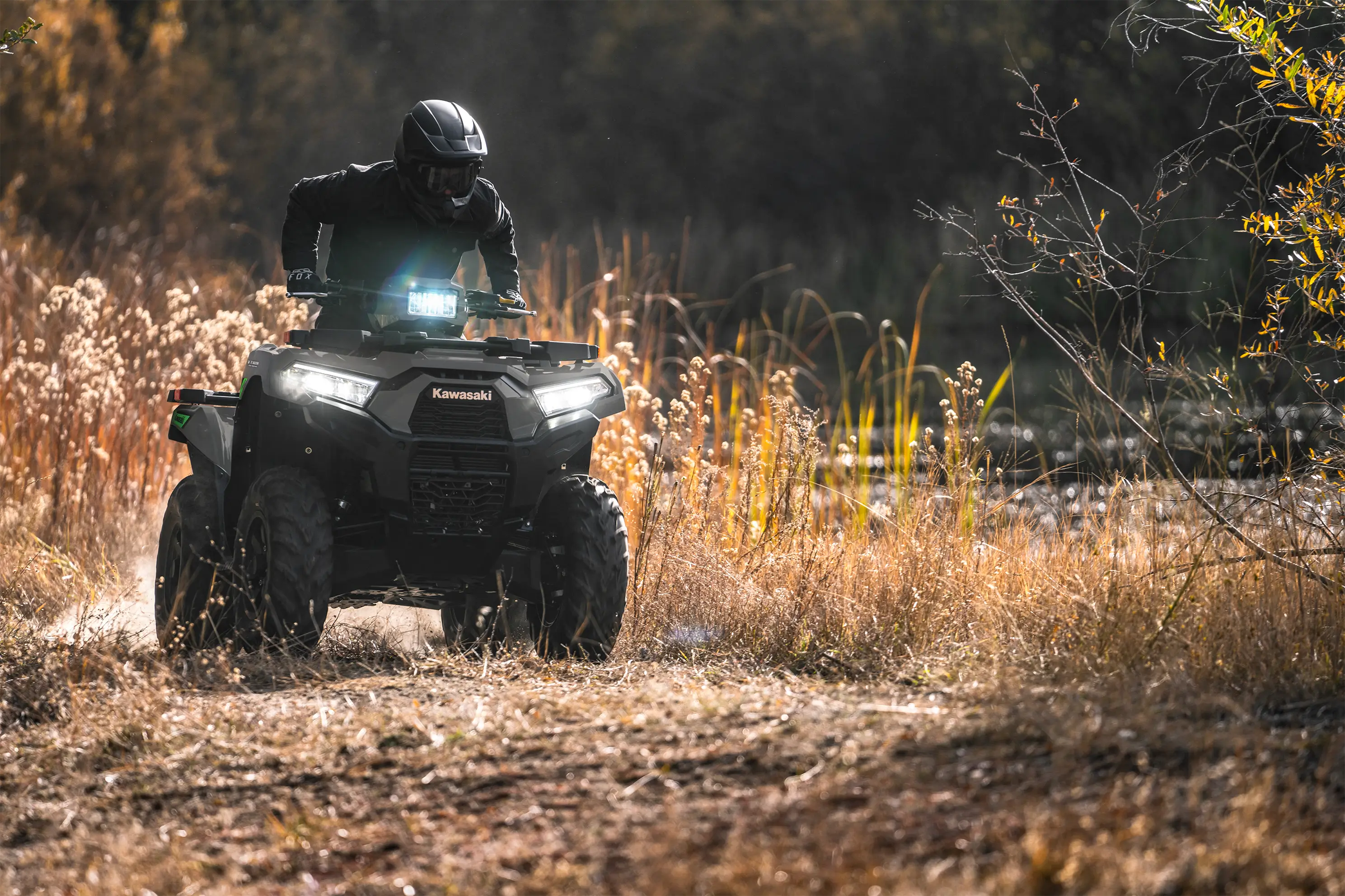 Person riding a utility UTV through a field with headlights on.