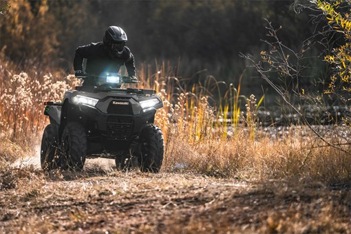 Person riding a utility UTV through a field with headlights on. opens in a new window