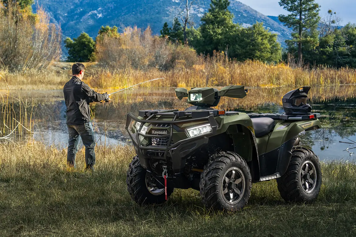 Utility ATV parked in front of a scenic lake with a person fishing in the background.