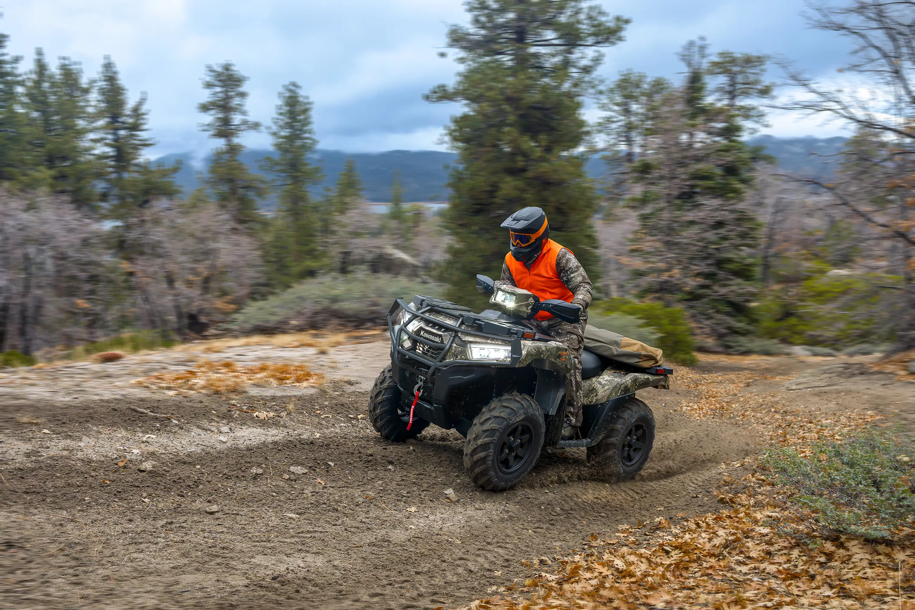 Person wearing camo and an orange vest riding a utility ATV on a road through the woods.