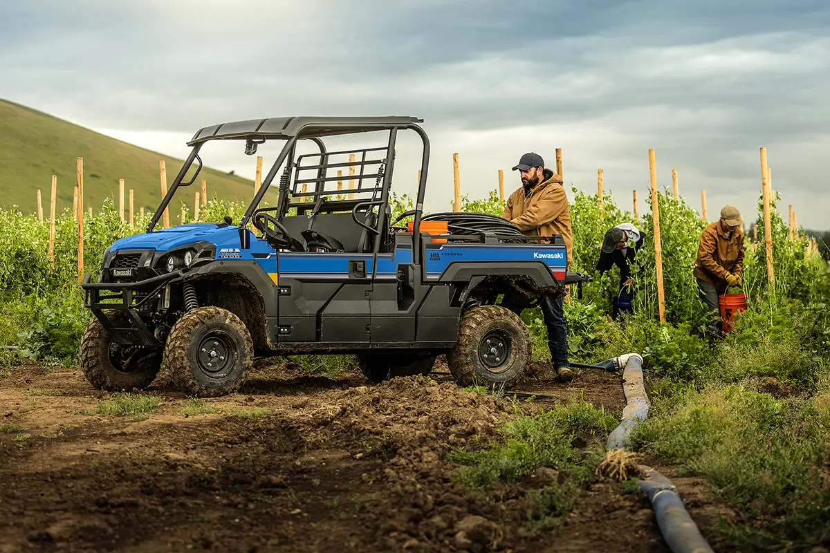 Blue side x side parked in front of rows of crops with people working.
