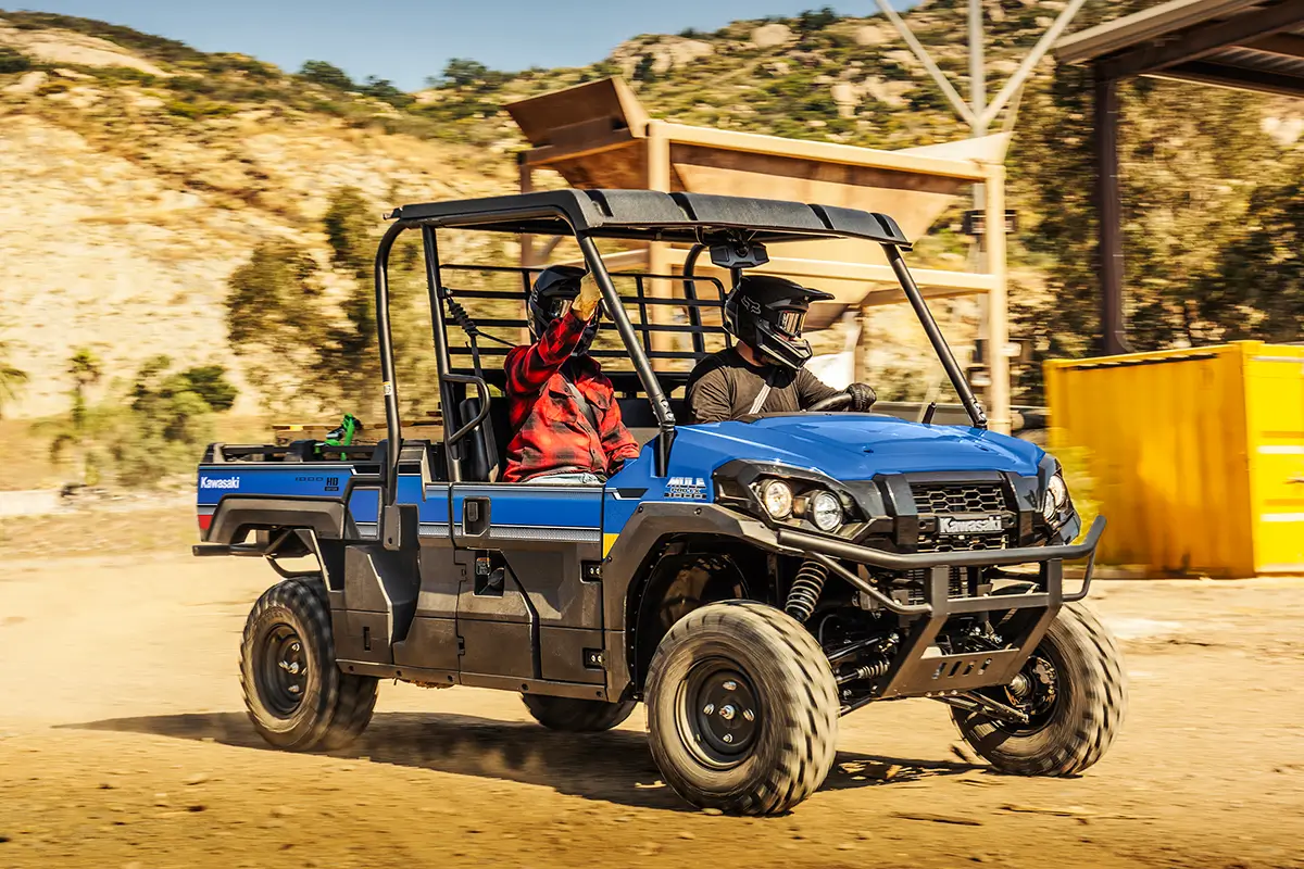 Two people riding in a blue side x side in front of farming equipment.