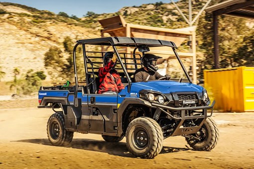 Two people riding in a blue side x side in front of farming equipment. opens in a new window