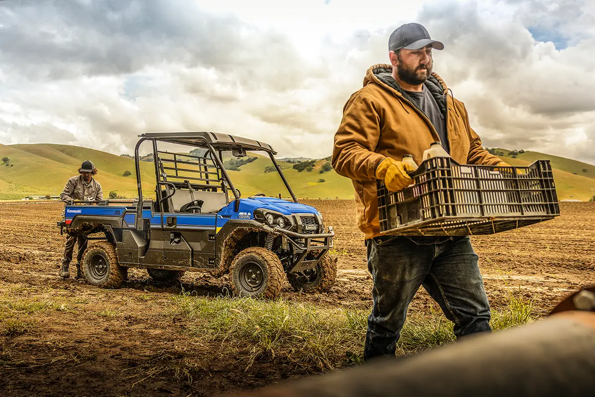 Person carrying a crate with a blue side x side in the background.