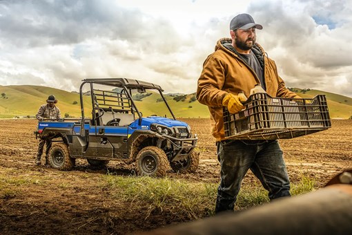 Person carrying a crate with a blue side x side in the background. opens in a new window