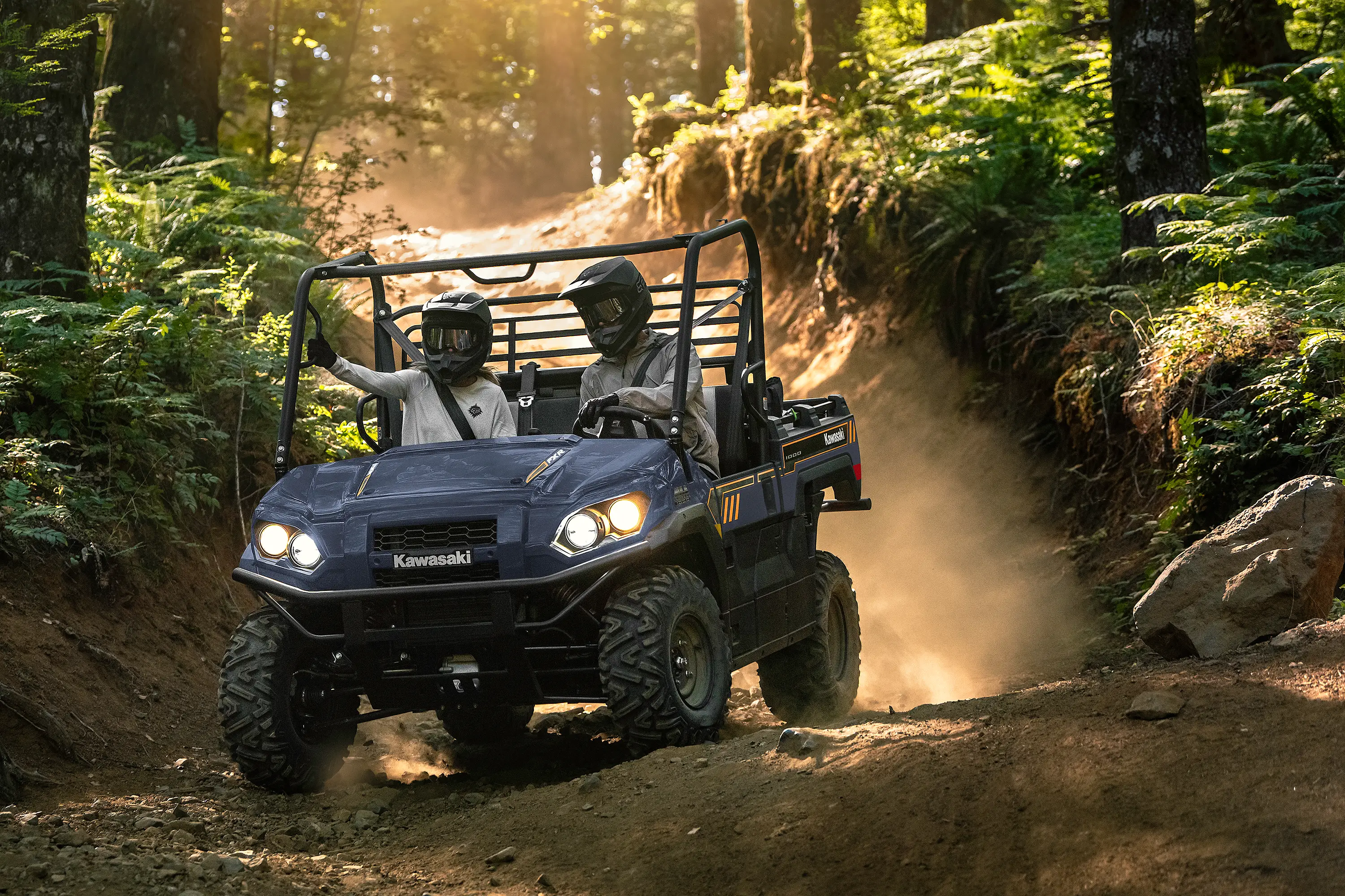 Oncoming view of two people riding in a side x side down a forest road.