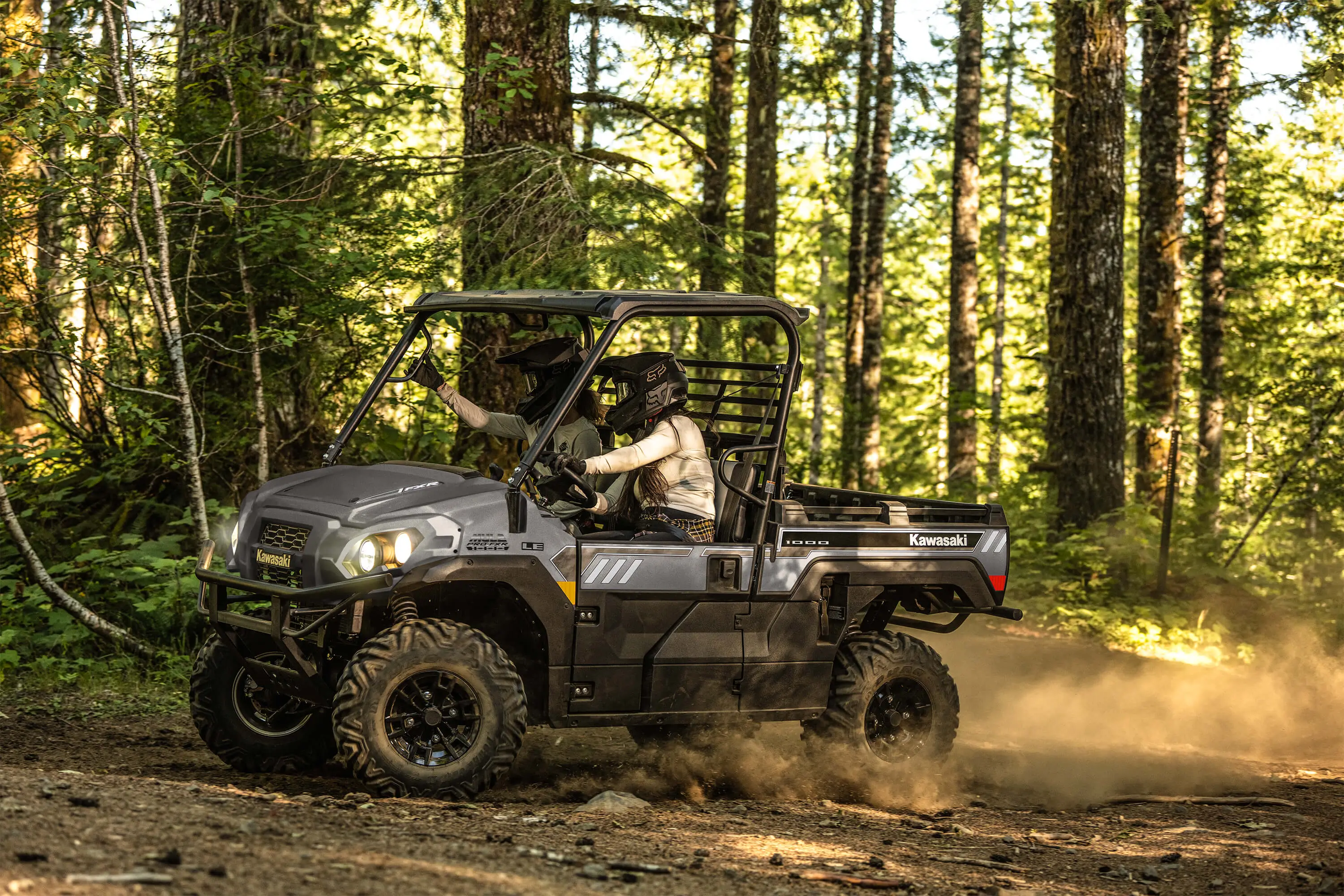 Left side view of two people riding in a side x side on a forest road.