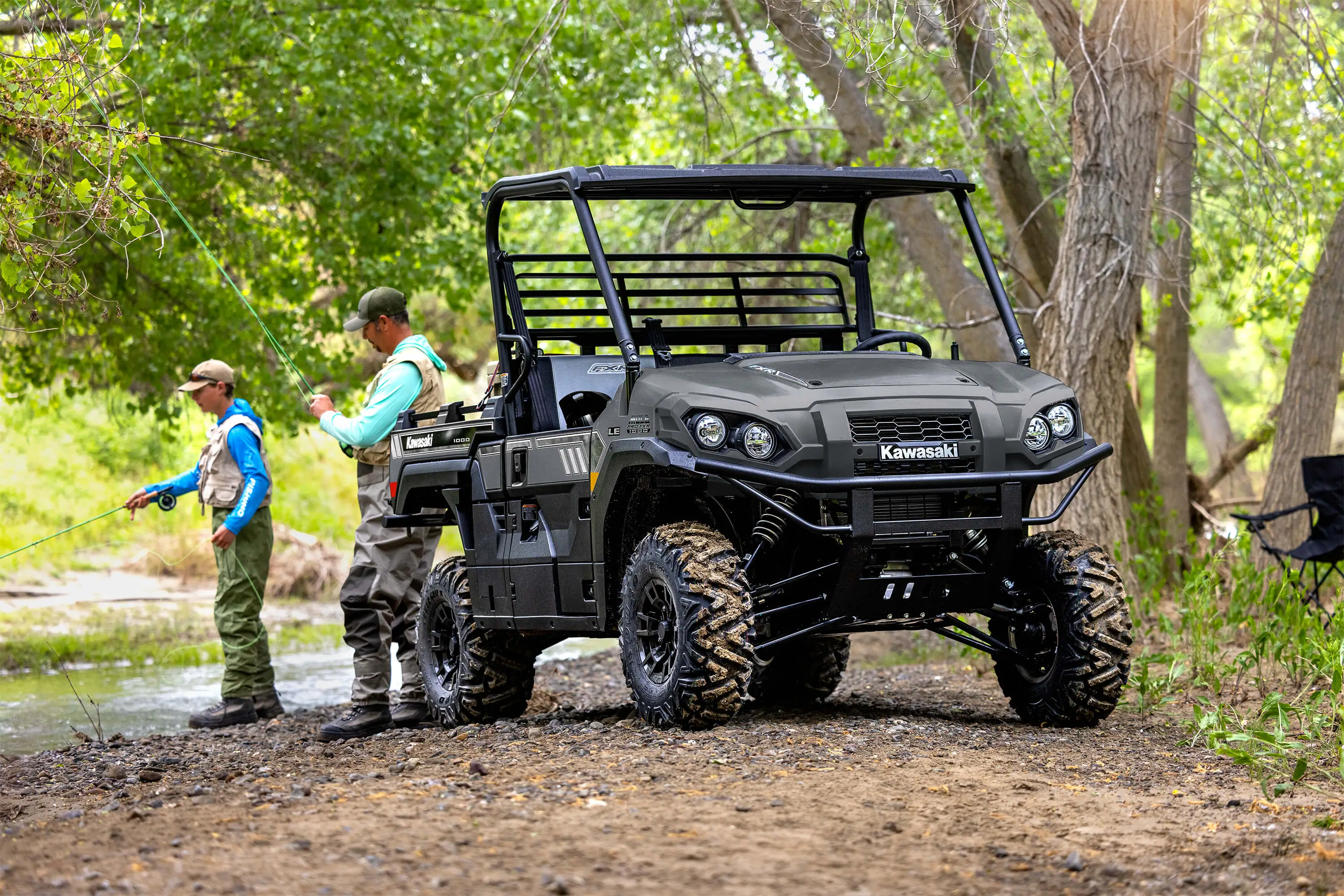 Side x side parked next to a stream with two people fishing in the background.