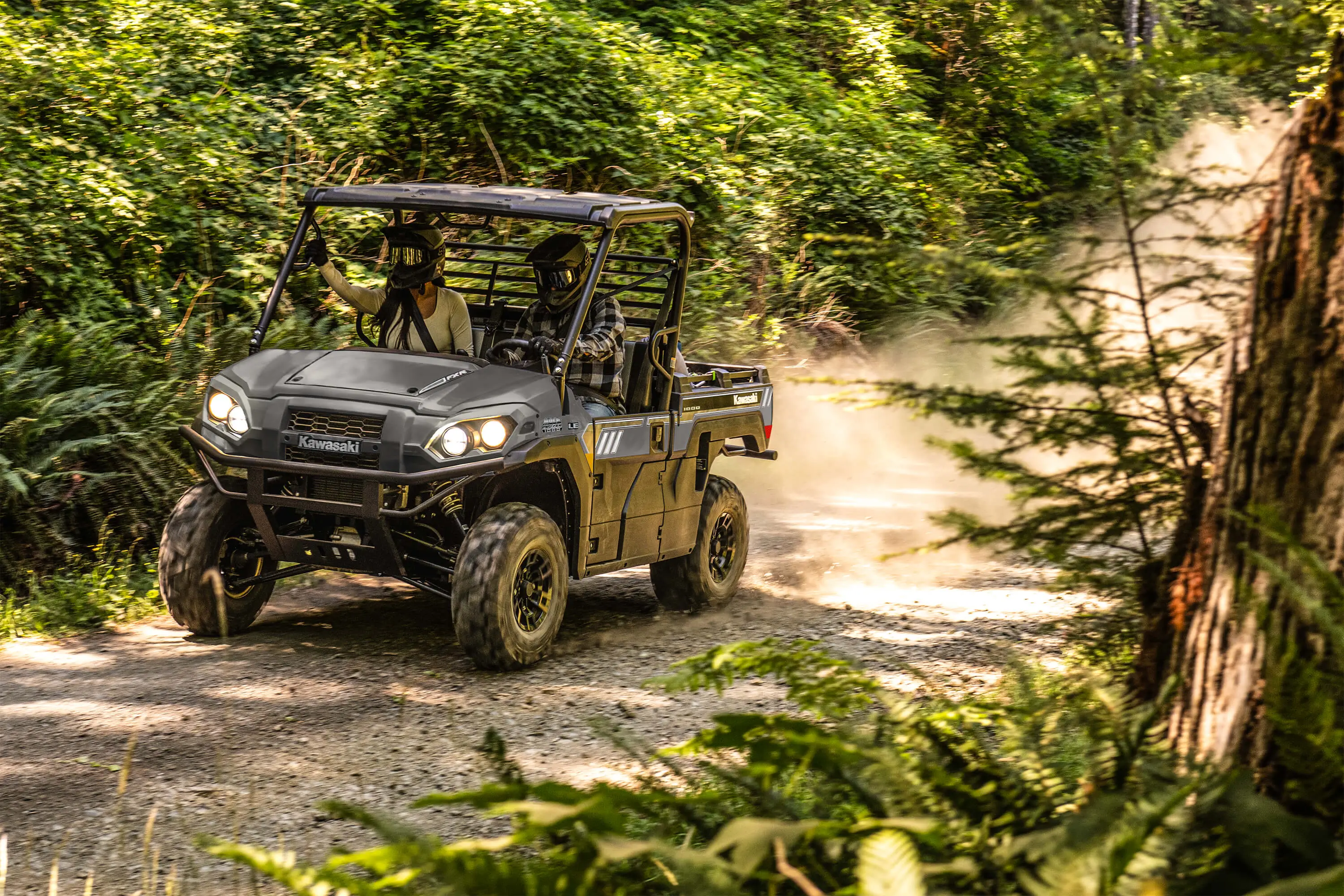 Front three-quarter view of two people riding in a side x side on a forest road.