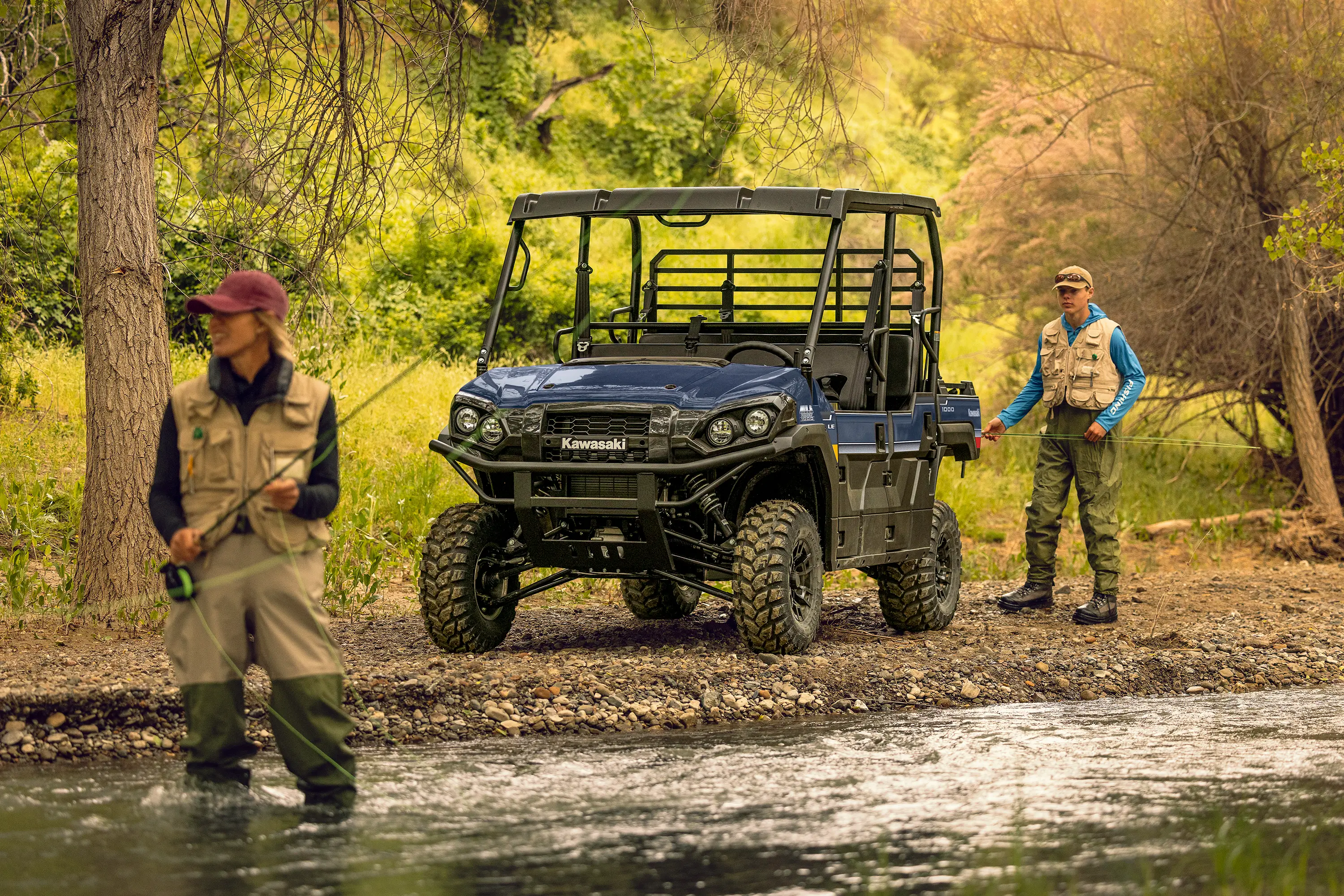 Two people fly fishing in a stream with a side x side parked in the background.