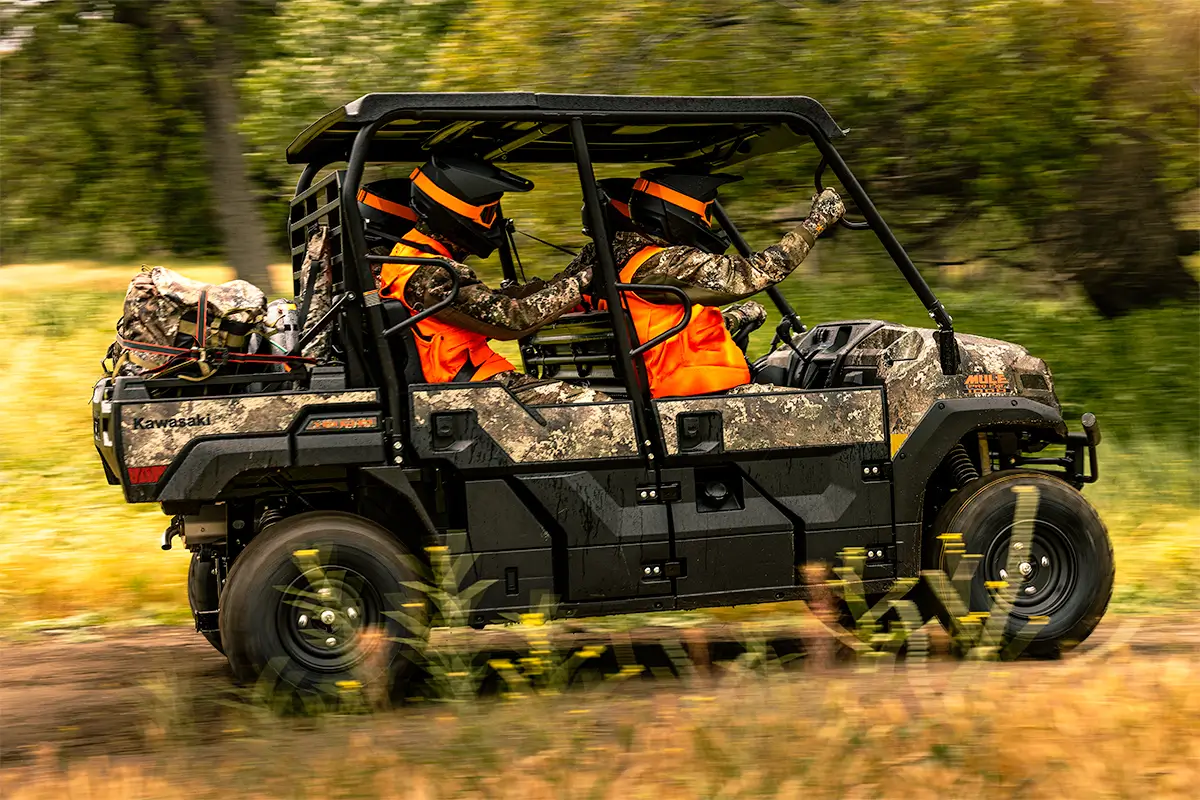 Right side view of people in orange vests riding in a side x side on a dirt road.