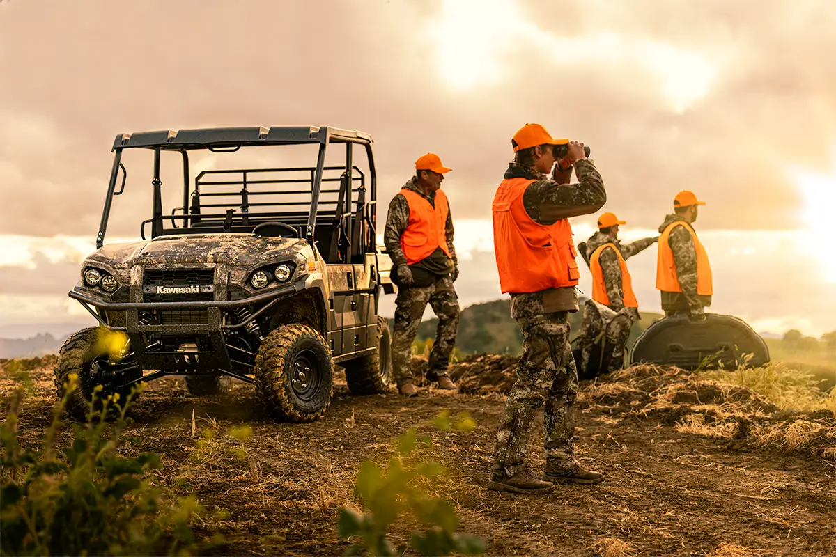 A group of people in orange vests near a side x side parked on a hilltop.