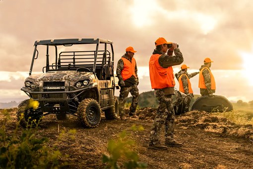 A group of people in orange vests near a side x side parked on a hilltop. opens in a new window