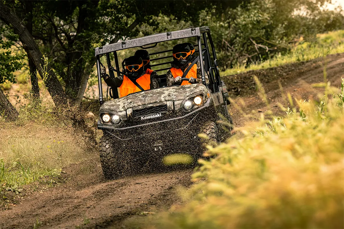 Oncoming view of people in orange vests riding in a side x side splashing through a puddle.