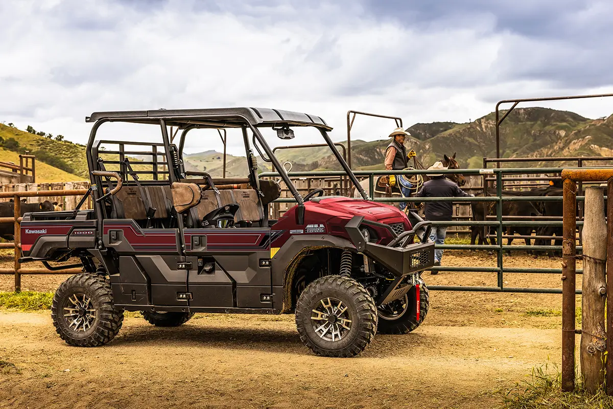 Red side x side parked near pipe corrals and cowboys in the background.
