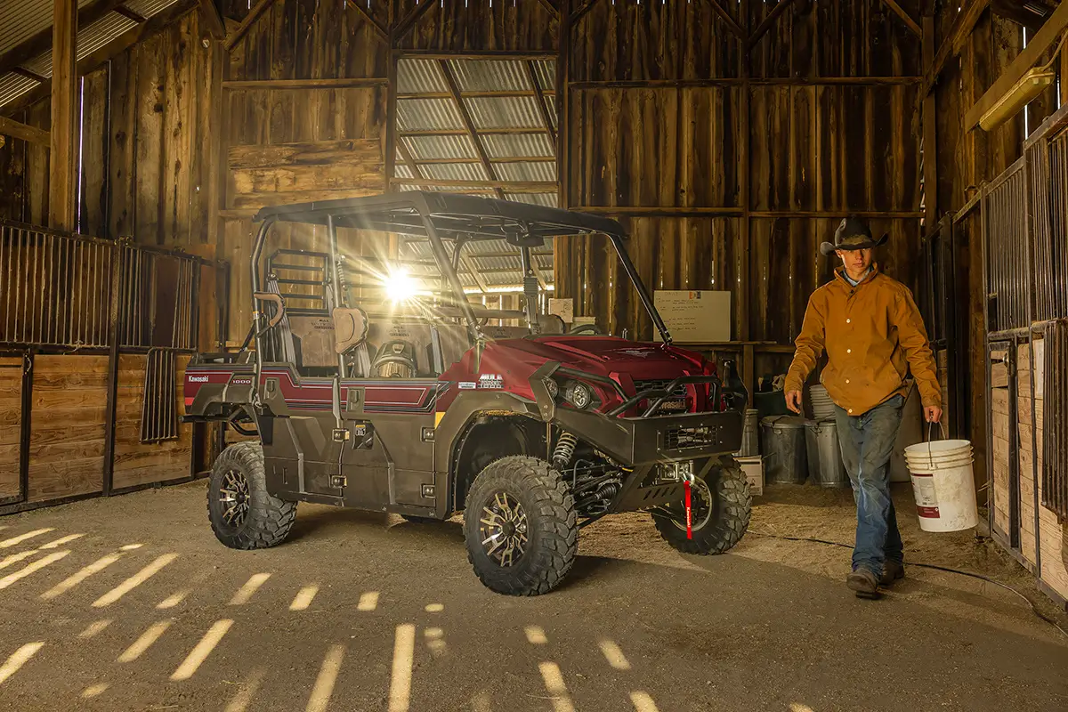 Red side x side parked inside a wood barn and a cowboy nearby.