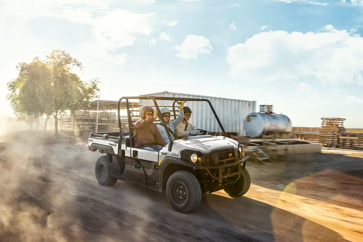 Three people riding in a side x side on a dusty ranch road.