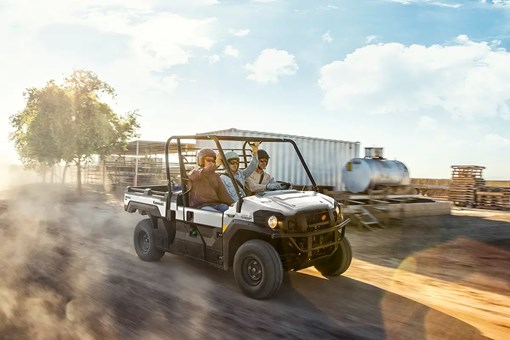 Three people riding in a side x side on a dusty ranch road. opens in a new window