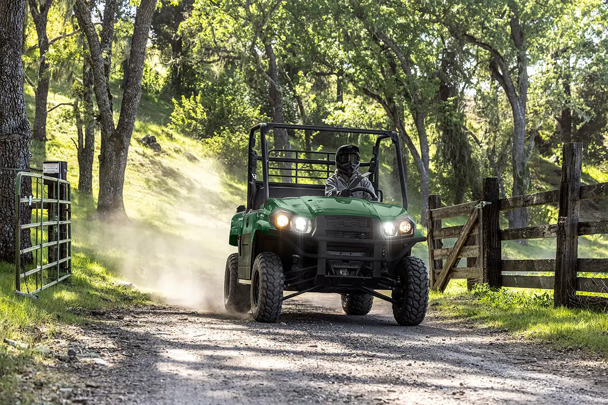 Person driving a green side x side down a dirt road under trees.