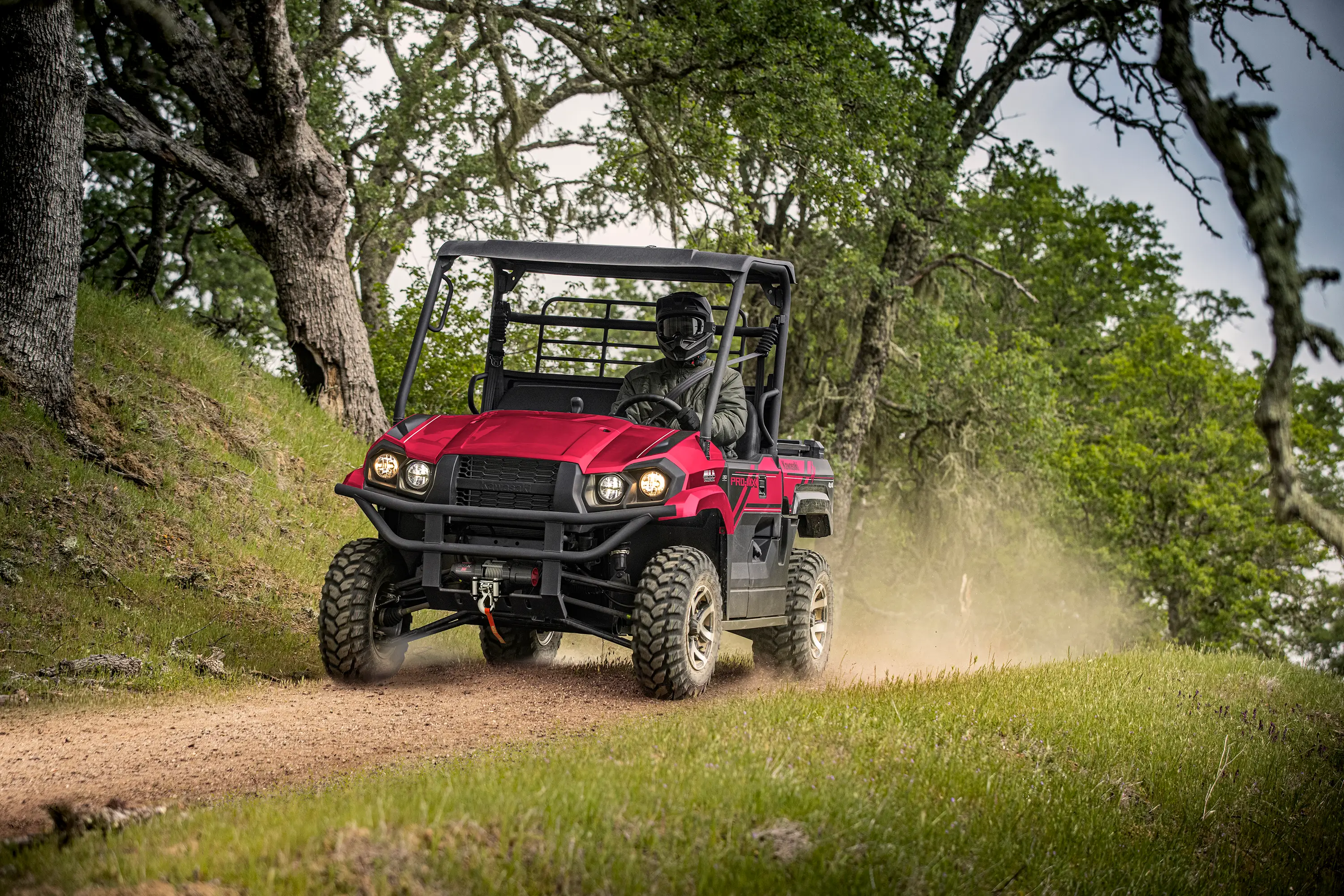 Person driving a red side x side down a dirt road under trees.