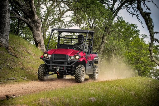 Person driving a red side x side down a dirt road under trees. opens in a new window