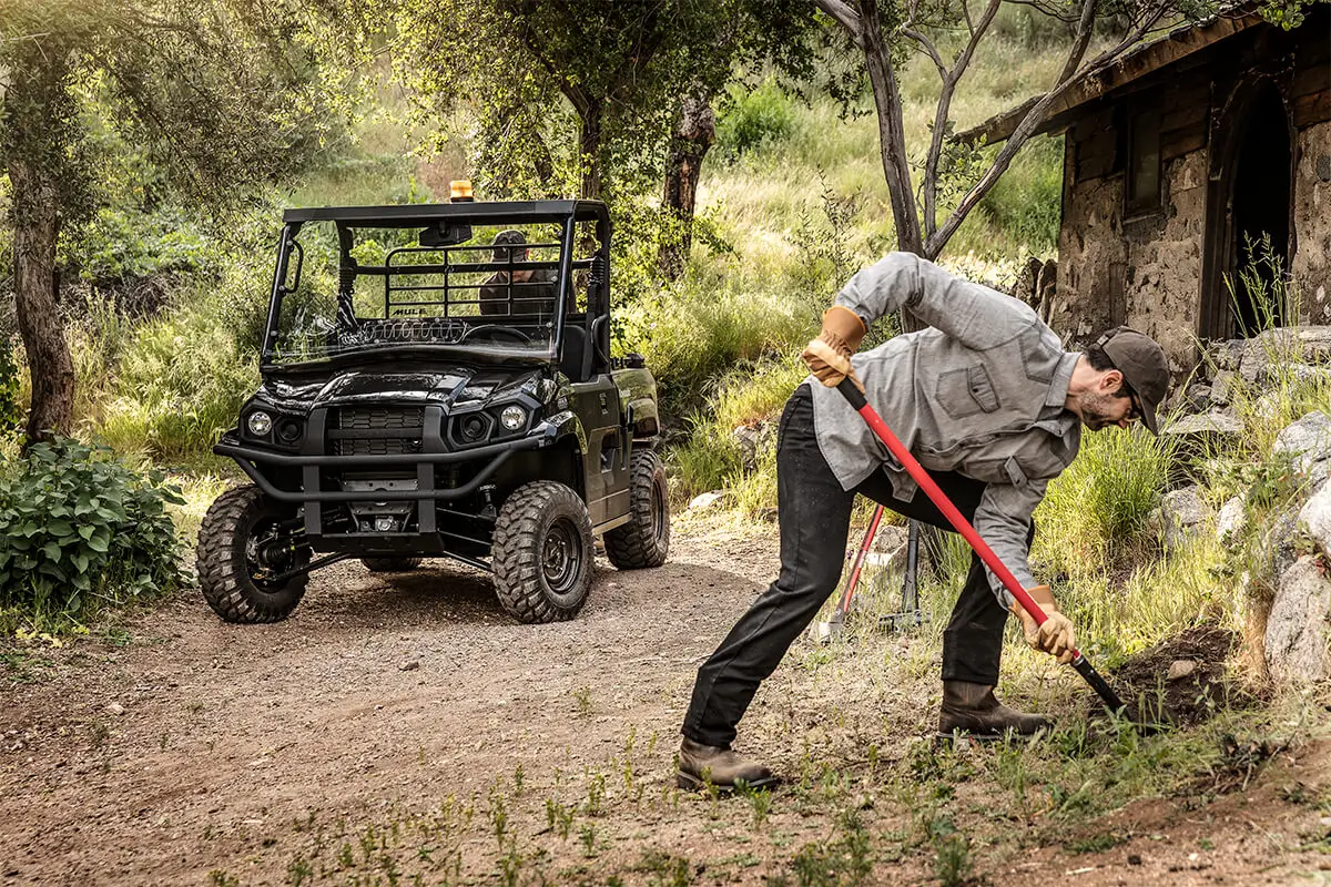 A person shoveling dirt in the woods near a side x side.