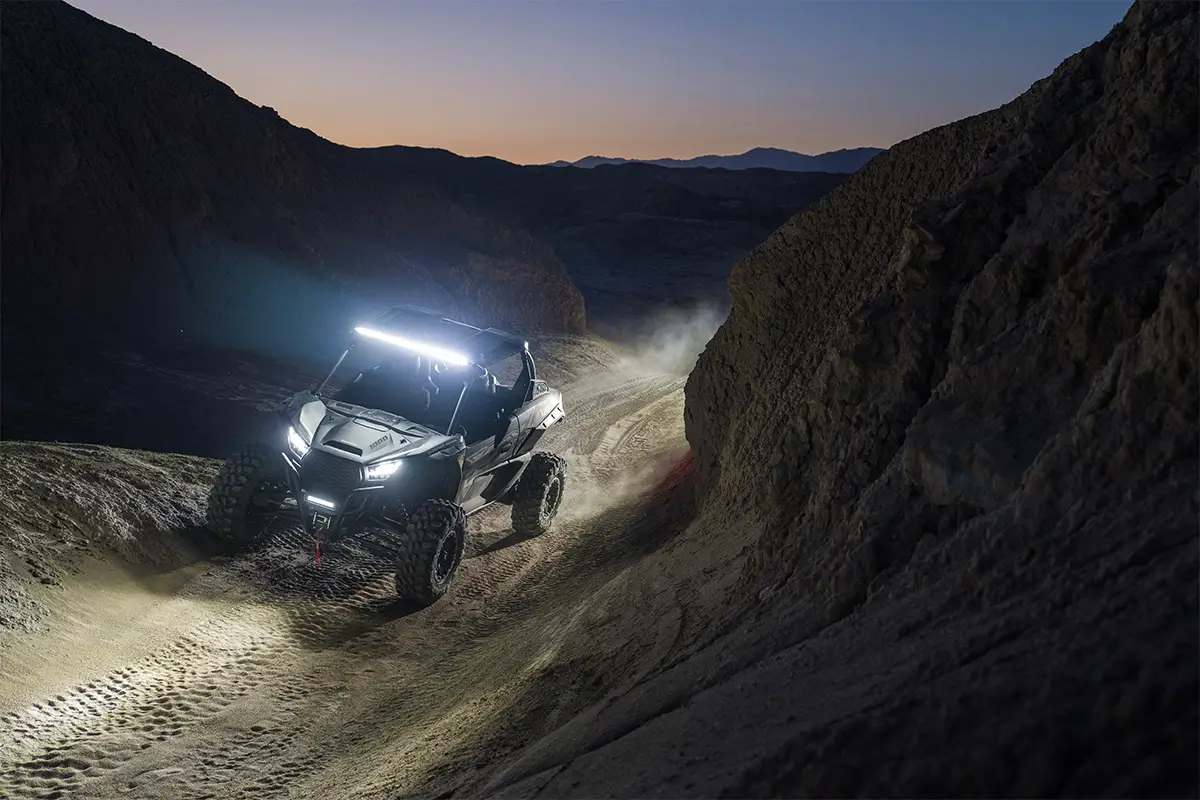 Three-quarter front angle of two people driving a side x side off-road.