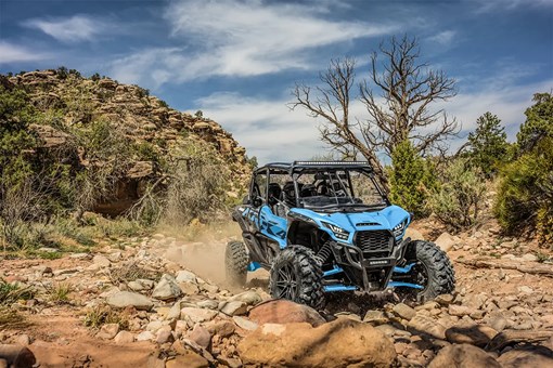 Three-quarter front angle of four people driving a side x side off-road. opens in a new window