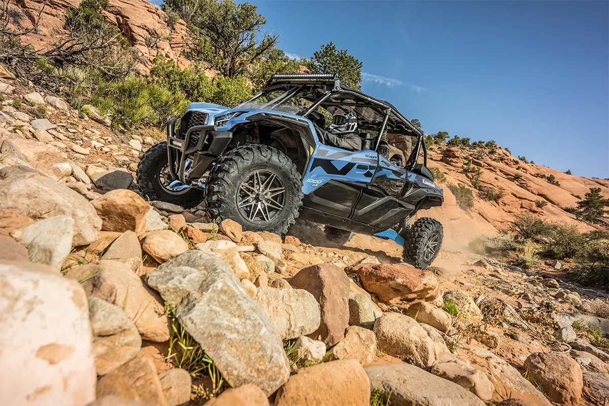 Side angle of three people driving a side x side off-road.