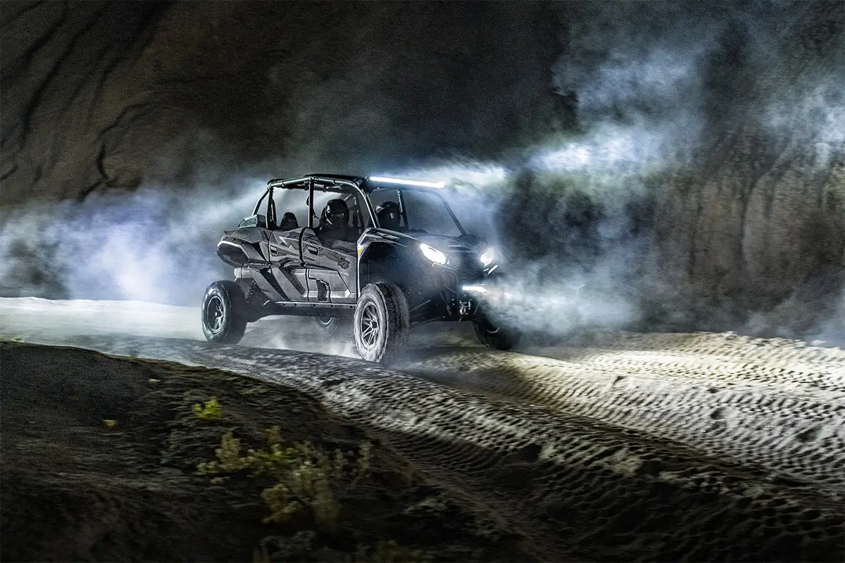 Three-quarter front angle of two people driving a side x side off-road.