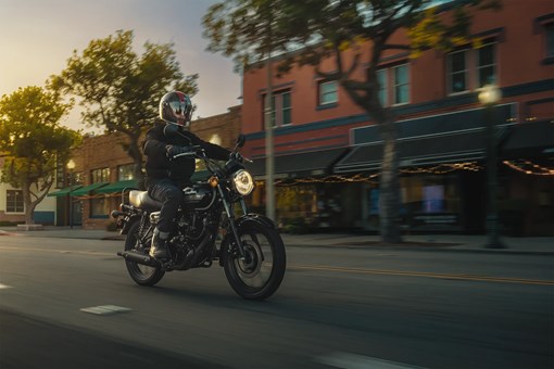 Three-quarter front angle of a person riding a motorcycle on a downtown street. opens in a new window