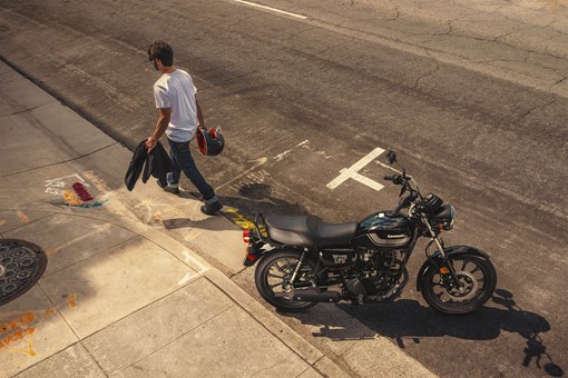 Aerial side angle of a person walking near a motorcycle parked in a downtown area. opens in a new window