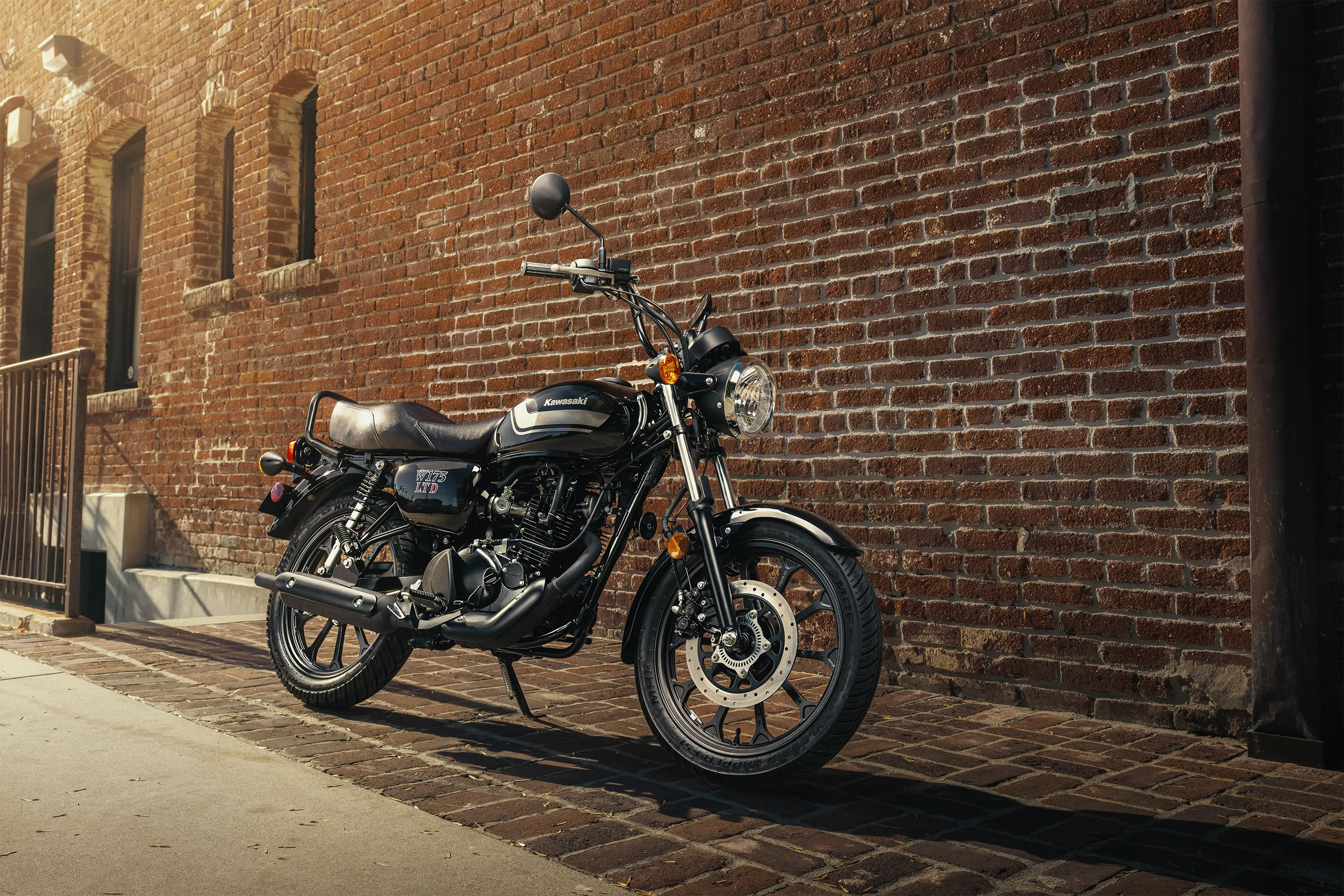 Side angle of a motorcycle staged next to a brick wall in a downtown area.
