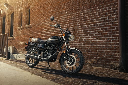 Side angle of a motorcycle staged next to a brick wall in a downtown area. opens in a new window