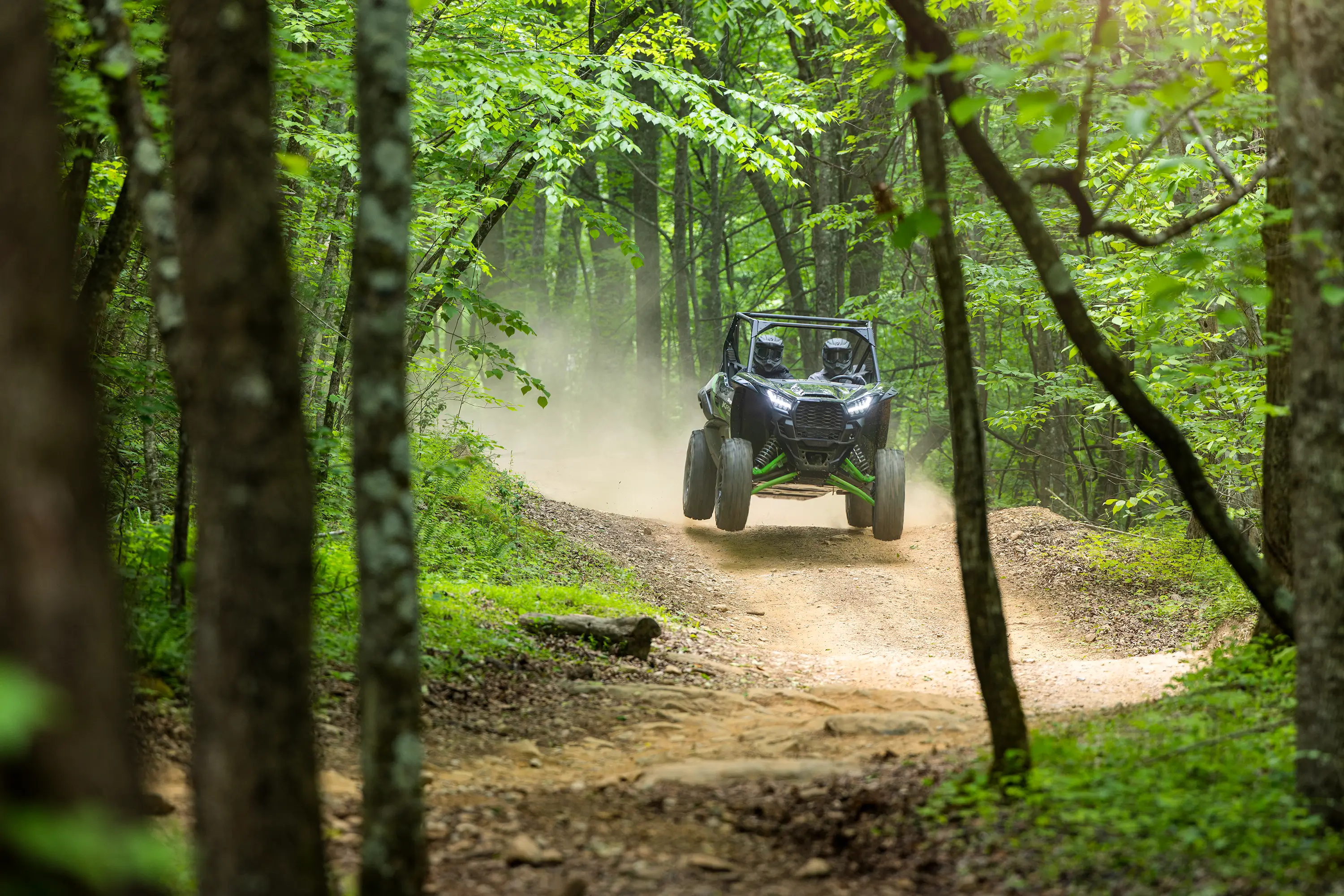 A driver and passenger riding a black side x side on a wooded trail.