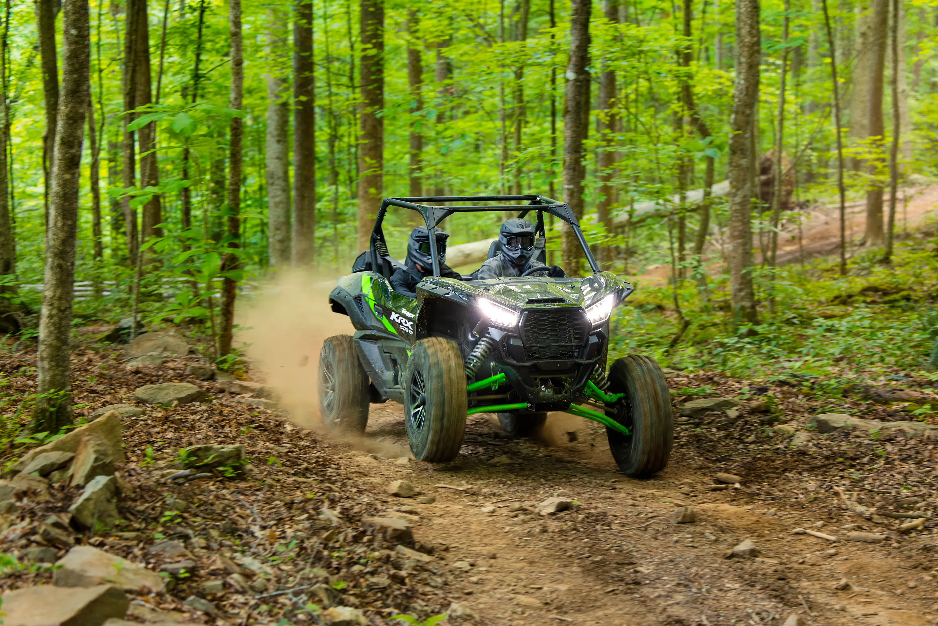 Three-quarter front angle of a driver and passenger riding a side x side on a wooded trail.