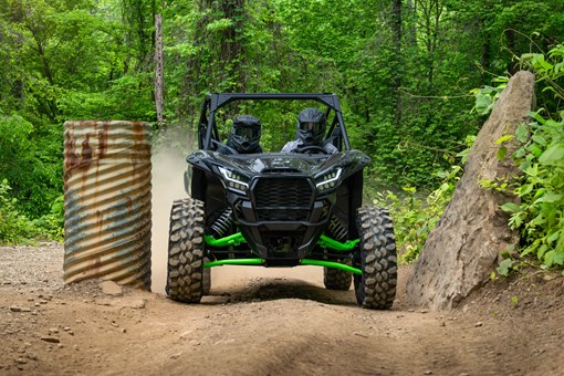 A driver and passenger riding a side x side on a wooded trail. opens in a new window