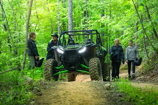 Front angle of a side x side parked on a forest trail near a group of riders. opens in a new window
